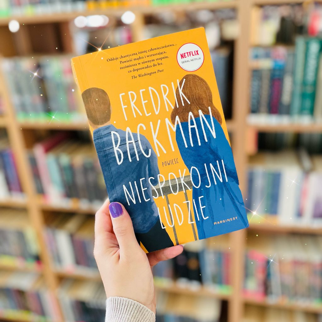Książka Fredrika Backmana "Niespokojni ludzie" trzymana w dłoni, widoczna na tle regału z książkami