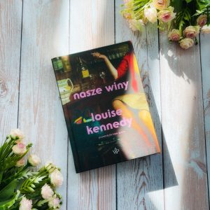 książka "Nasze winy" Louise Kennedy leży na blacie z desek, obok niej bukiety róż